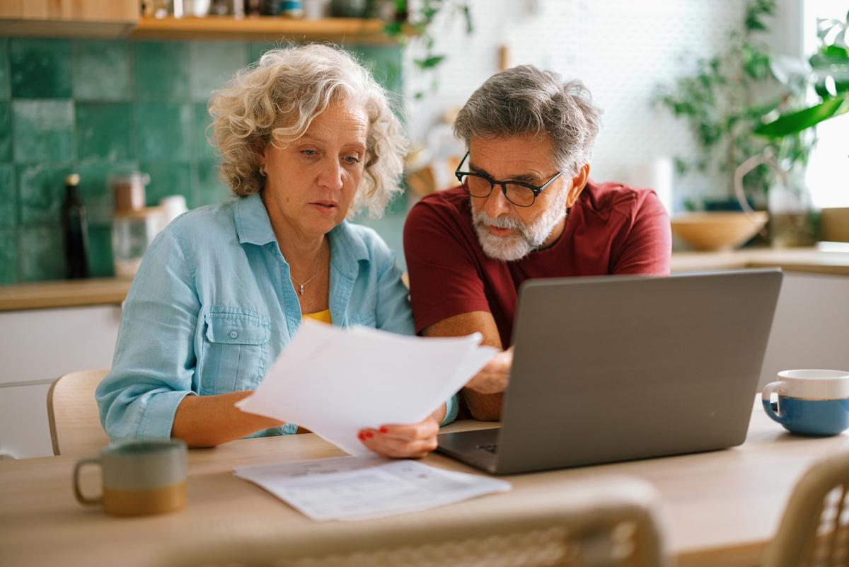 Senior couple paying bills and managing family finances together on a laptop, discussing expenses at home.