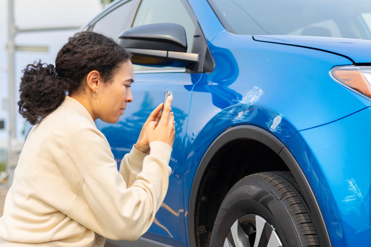 Woman is inspecting a damaged car and taking a picture of it.