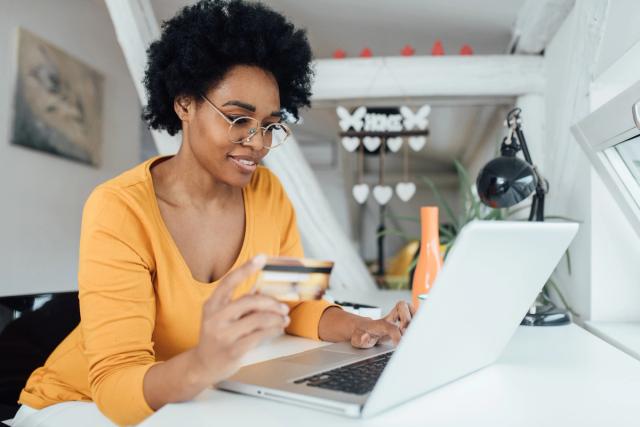 Woman online shopping at home using her credit card to pay.