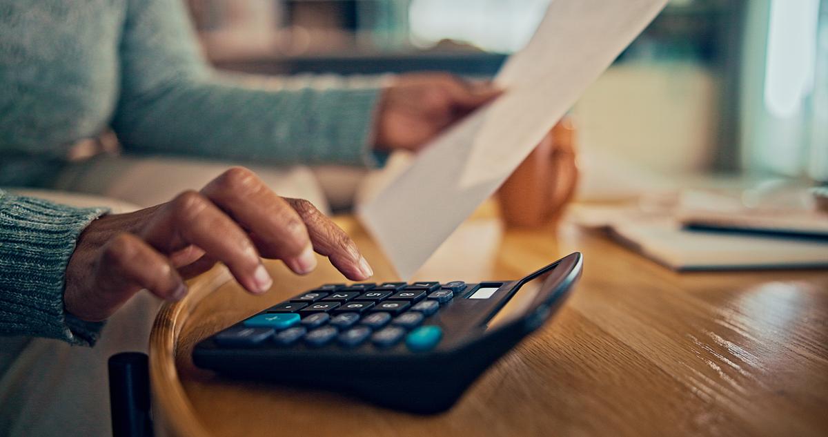 Person sitting at desk budgeting their finances using a calculator.