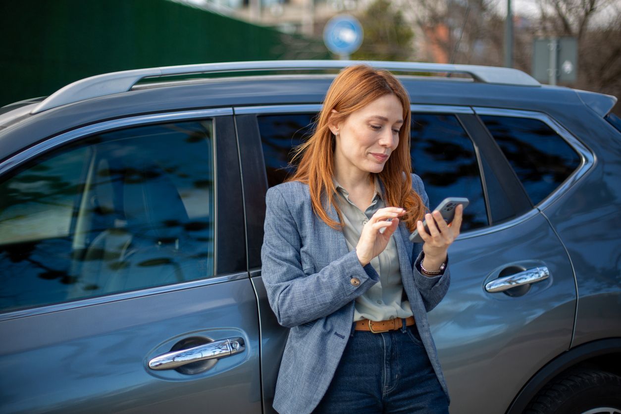 Woman using smartphone standing next to her car on an urban street.