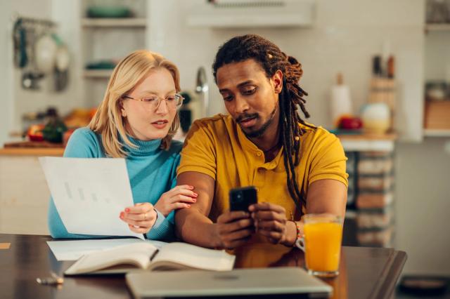Couple looking at phone at home, using online banking services and checking finances.