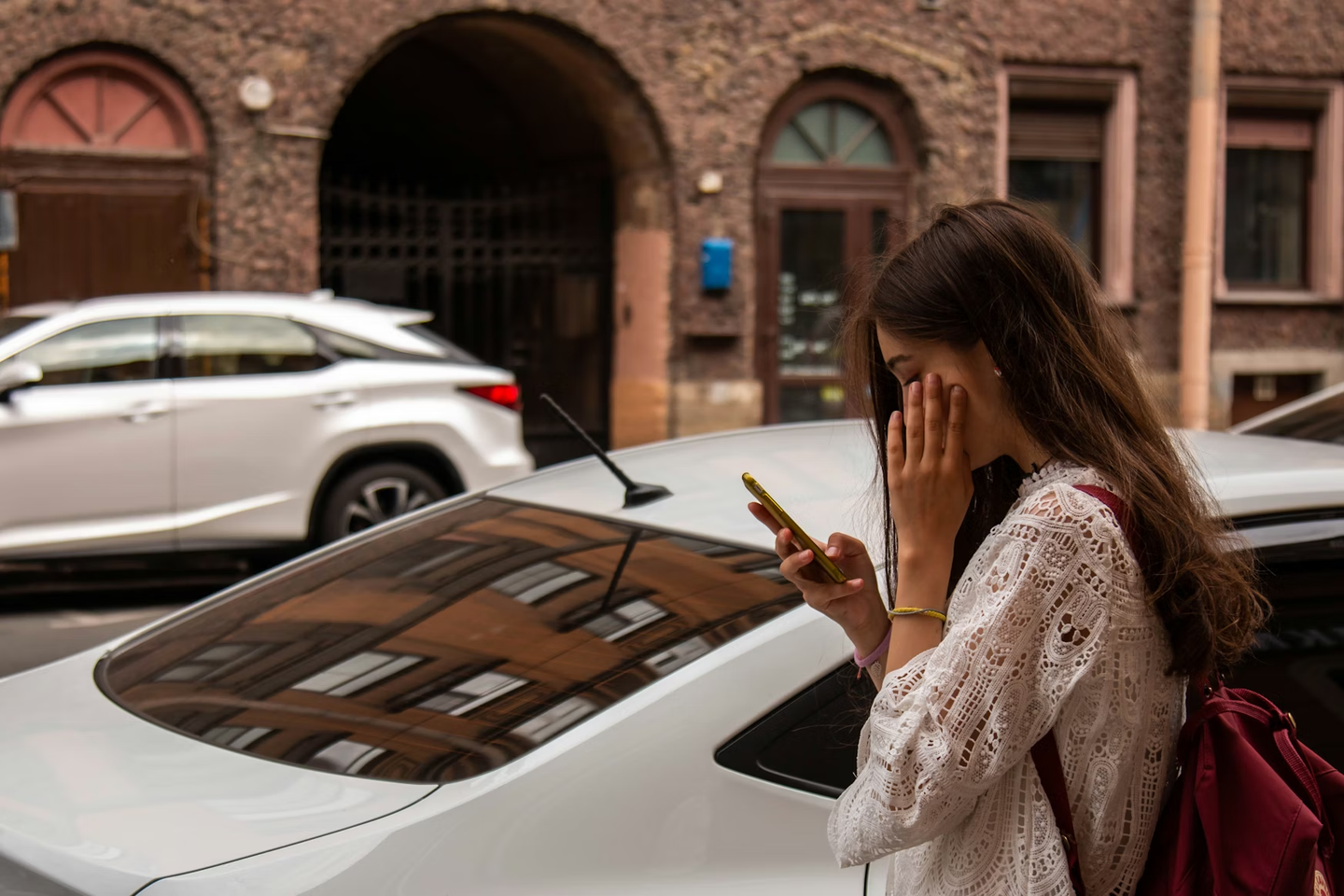 Woman looking at her phone next to a parked car