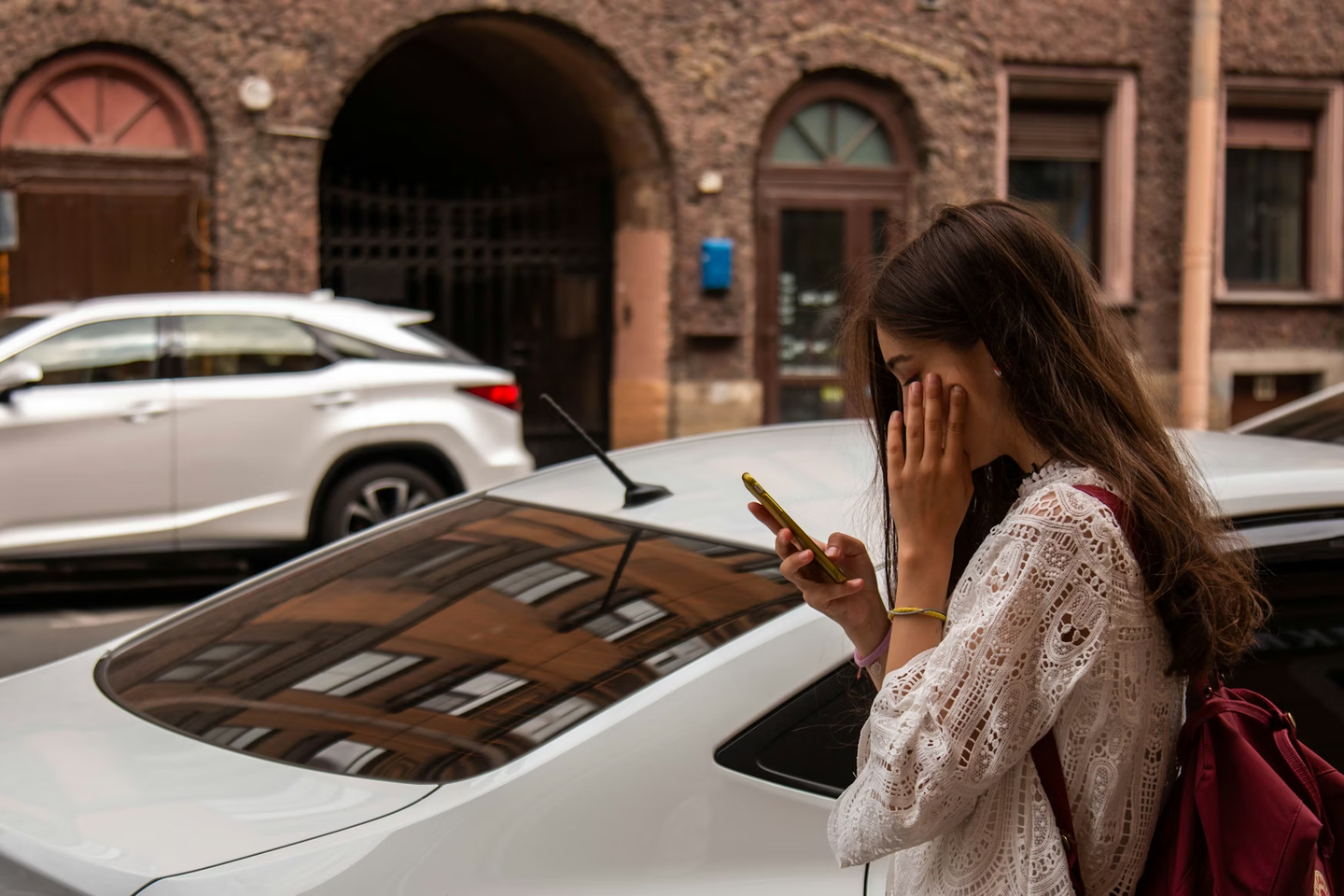 Woman looking at her phone next to a parked car