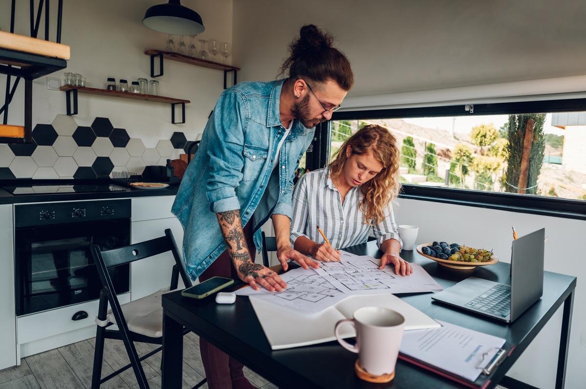 Young couple working on blueprints of house renovation while sitting at table in the kitchen.