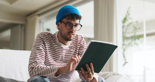 Young man sitting on a couch and checking his tablet
