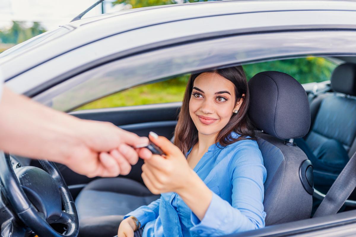 Close up image of a hand passing passing car keys to a female driver.